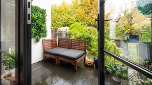 En træbænk med puder på en balkon med udsigt over en have og træer.