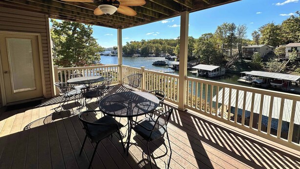 A covered outdoor deck with a table and chairs, overlooking a lake with boats and docked houses. - Lake It Easy - Waterfront Getaway With 7 Bedrooms! (Rocky Mount)