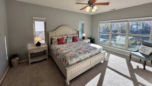 A bedroom with a bed, a nightstand, a lamp, a ceiling fan, and a window with a view of the outside. - Lake It Easy - Waterfront Getaway With 7 Bedrooms! (Rocky Mount)