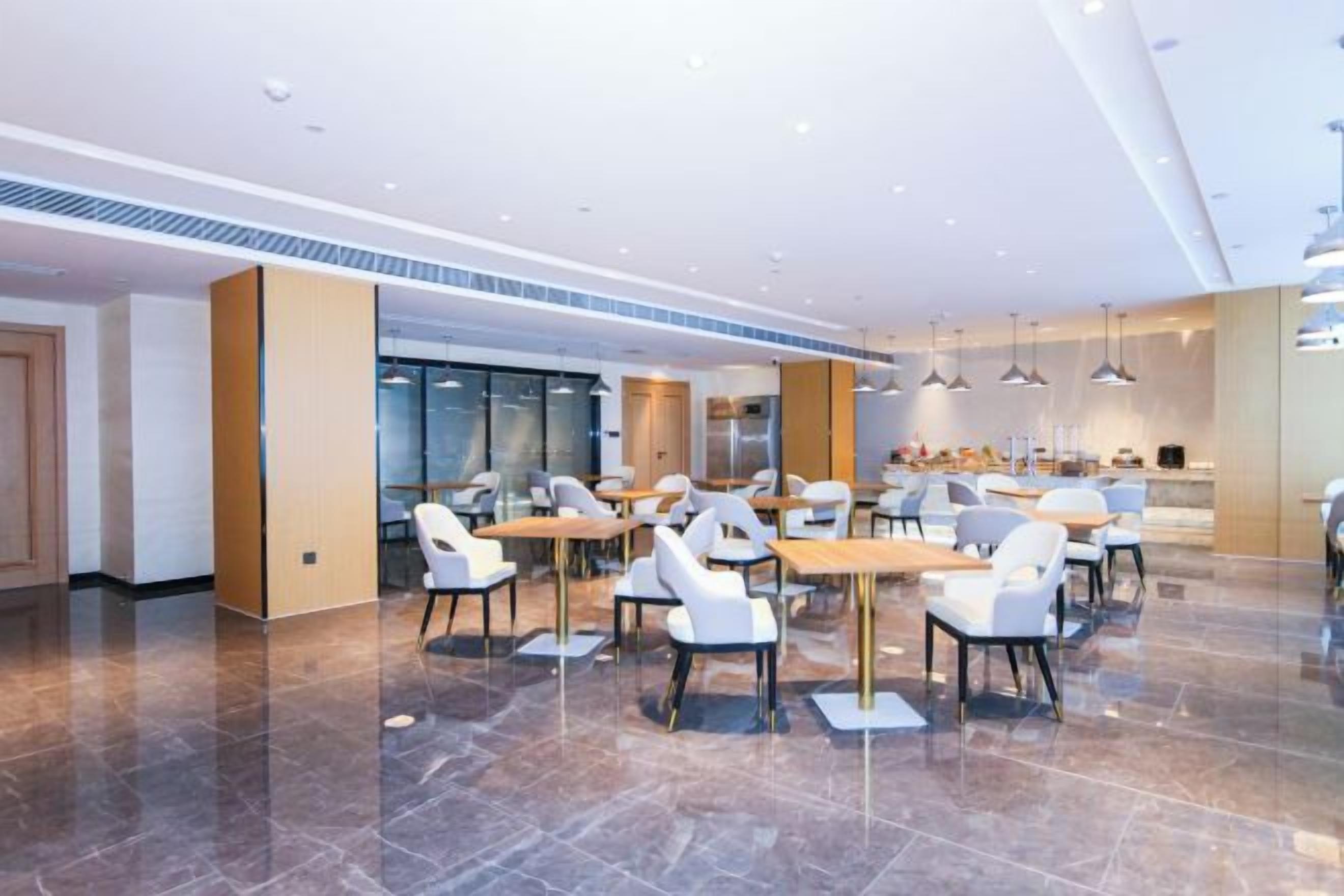 A modern dining area with tables and chairs, a kitchen in the background, and a polished floor.