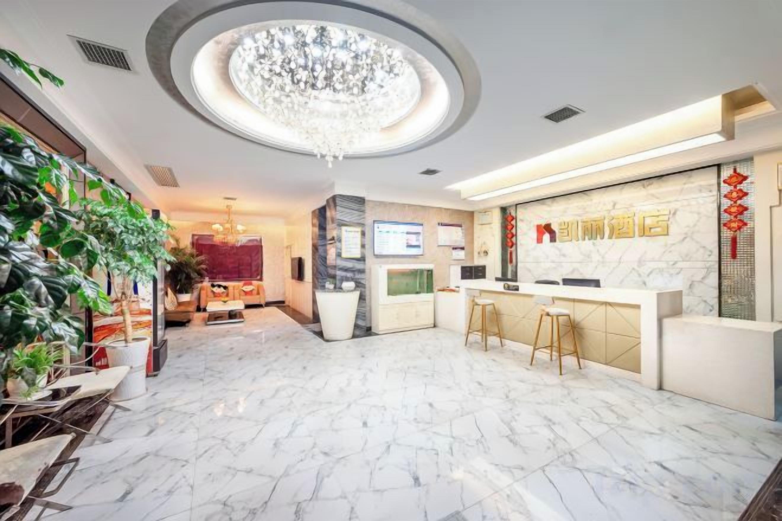 A hotel lobby with a marble floor, a reception desk, a chandelier, and a TV screen.