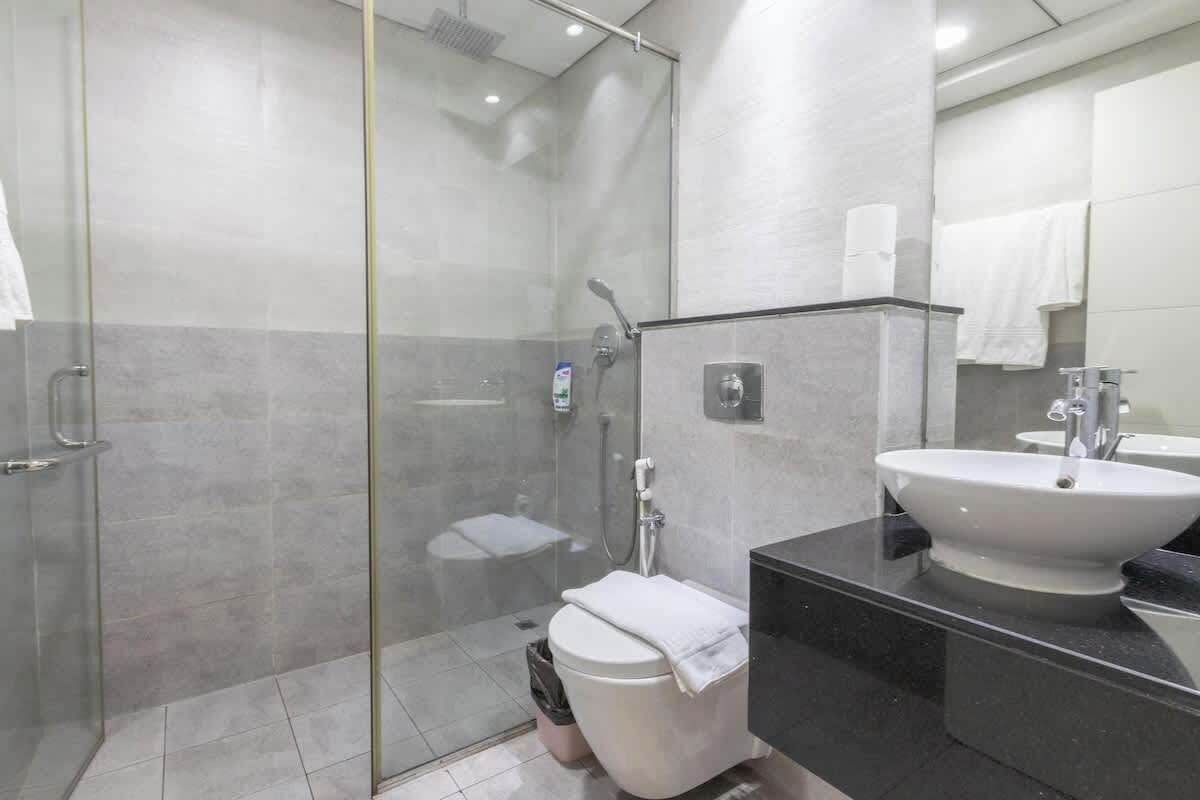 Une salle de bain moderne avec une douche à parois de verre, des toilettes blanches et un plan de toilette noir surmonté d’un lavabo blanc.