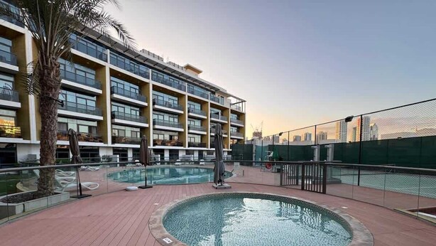 A rooftop pool area with a circular pool, palm trees, and a modern building with balconies in the background.