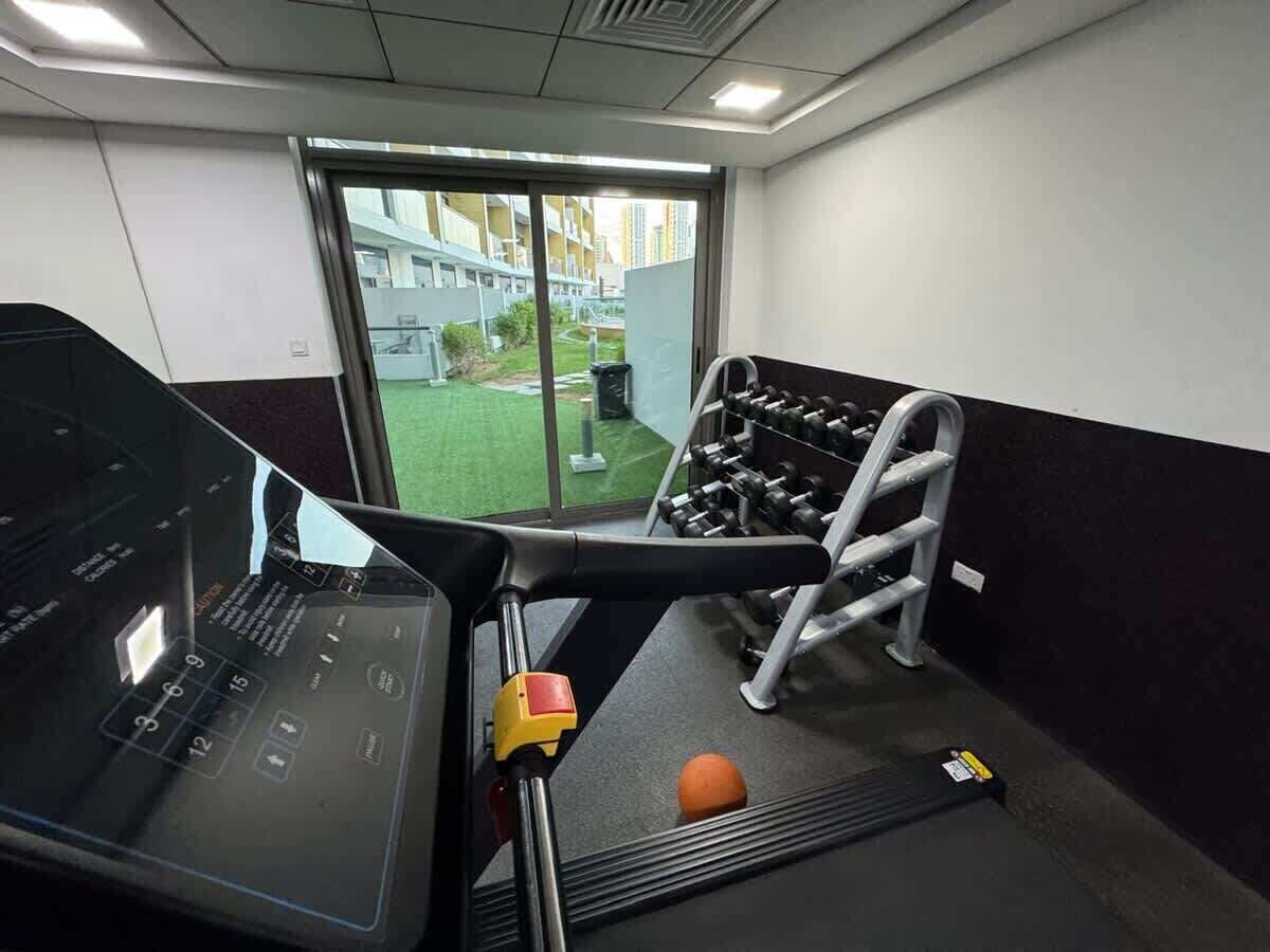 A gym with exercise equipment, a treadmill, and a view of a building outside.
