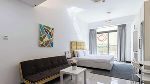 A modern hotel room with a bed, a sofa, a small table, and a painting on the wall.