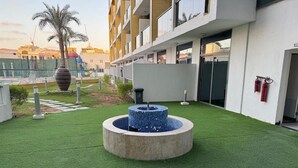 A courtyard with artificial green turf, a circular water feature, and a modern building with balconies.