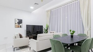Un salon moderne comprenant un canapé, un téléviseur à écran plat, une table à manger avec des chaises et une grande fenêtre avec des rideaux.