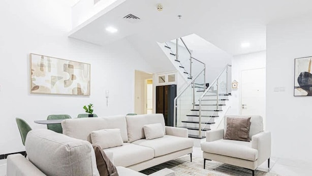 Un salon moderne avec un ensemble de canapés blancs, un escalier en verre et des œuvres d’art abstraites accrochées au mur.
