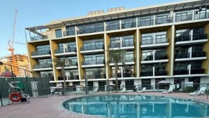 Un bâtiment moderne doté d’un espace piscine, de nombreux balcons et offrant une vue sur un ciel dégagé.
