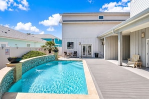 Uma piscina com deck de madeira, área de estar coberta e um edifício com fachada branca.