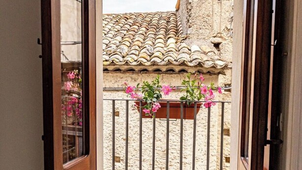A balcony with a tiled roof, a wrought iron railing, and a flower box with pink flowers. - Alborghetto2 (Gerace)
