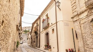 A narrow cobblestone street flanked by historic buildings with balconies and potted plants. - Alborghetto2 (Gerace)