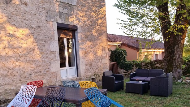 An outdoor seating area with a stone building, a table with chairs, and a tree. - GÎTE SARAZAC (Mayac)
