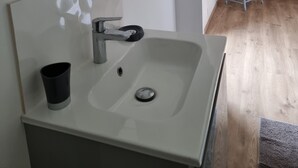A bathroom with a white sink, a mirror, and a blue chair in the adjacent room. - GÎTE SARAZAC (Mayac)
