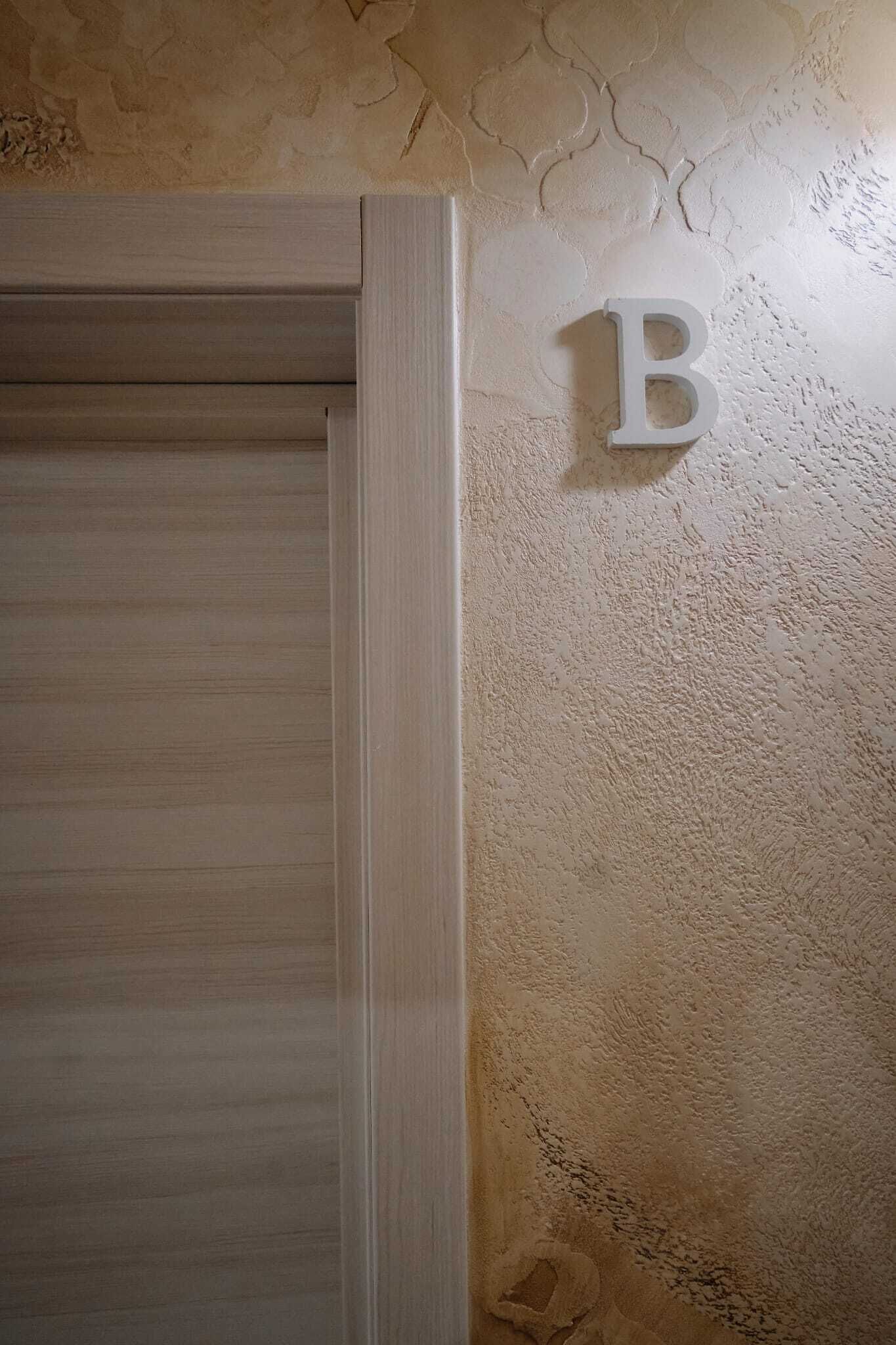 A wooden door with a textured wall and a letter 'B' mounted on it.