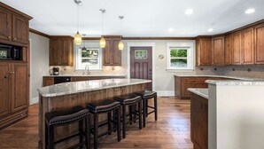 A modern kitchen with wooden cabinets, a large island with bar stools, and pendant lighting. - Lakeside Oasis Room for 12! (Linn Creek)