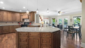 A spacious kitchen with wooden cabinets, granite countertops, and pendant lighting. - Lakeside Oasis Room for 12! (Linn Creek)