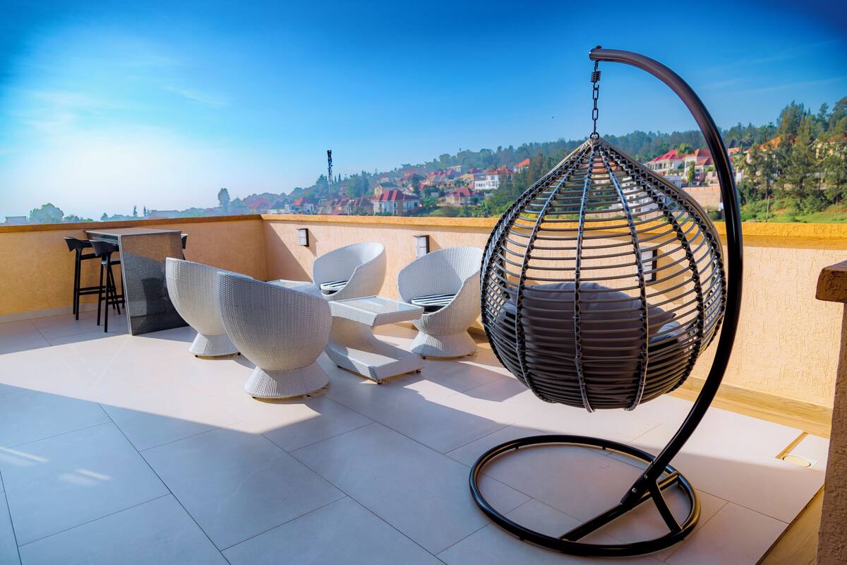 A rooftop terrace with white wicker furniture, including a hanging chair and a table with chairs.