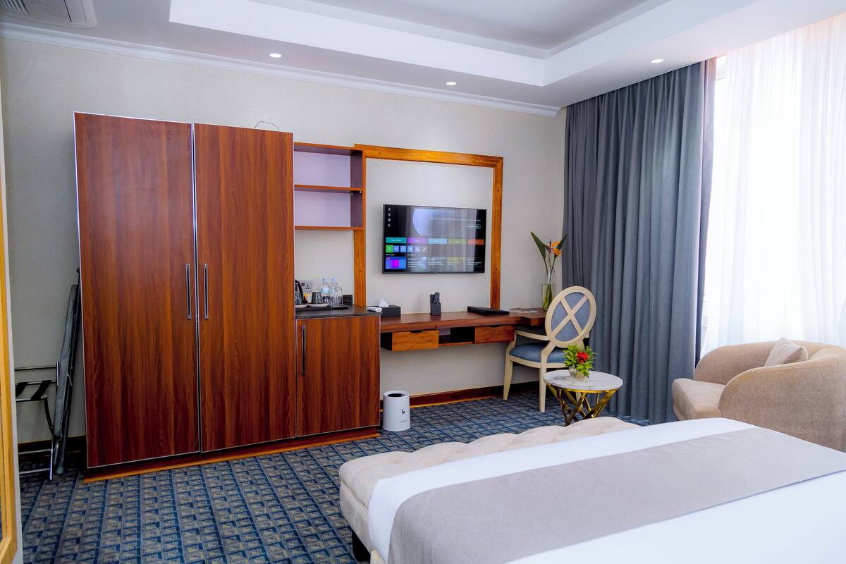A hotel room with a bed, a desk with a computer monitor, a wardrobe, and a seating area with a chair and a sofa.