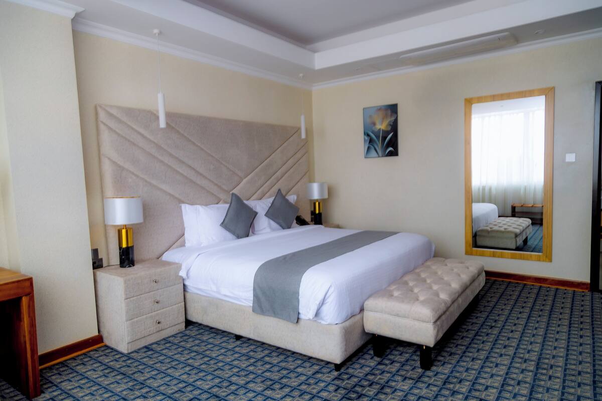 A hotel room with a large bed, bedside tables, a mirror, and a patterned carpet.