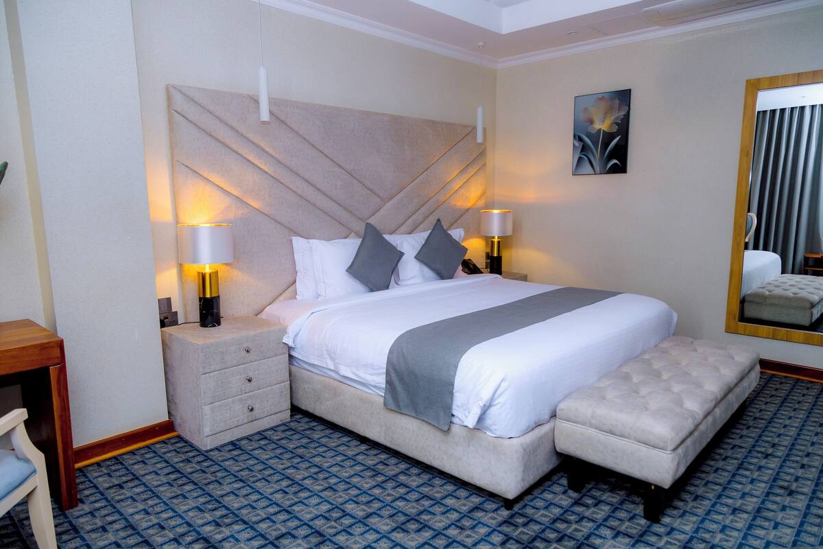 A neatly arranged hotel room with a large bed, two bedside tables with lamps, a small seating area, and a large mirror.