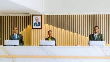 Three receptionists at a reception desk with laptops, a framed picture on the wall, and a striped background.