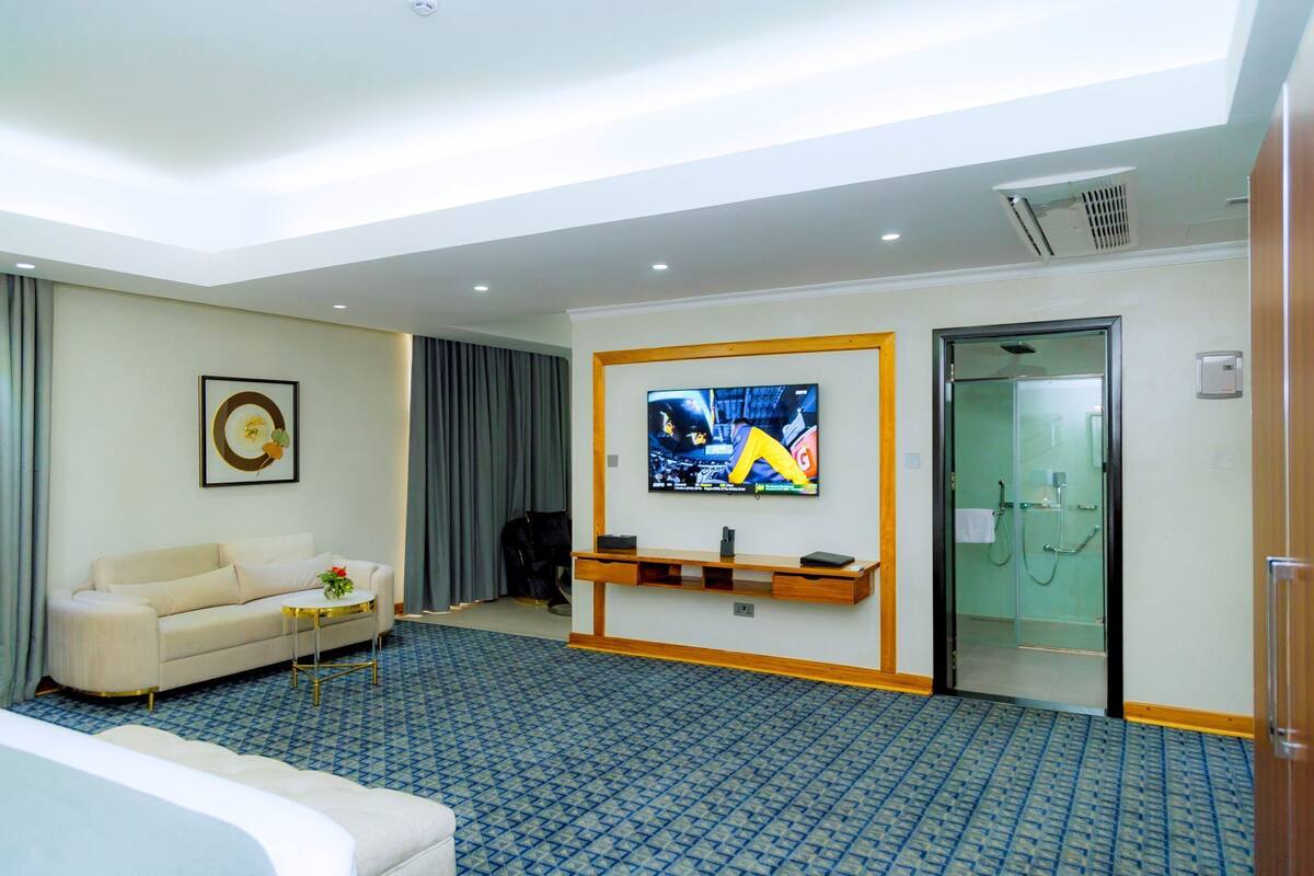 A hotel room with a sofa, a television, a small table, and a glass-enclosed shower.