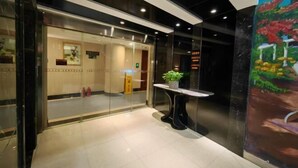 Un hall d’hôtel avec un comptoir d’accueil, une entrée avec une porte en verre et une plante en pot.