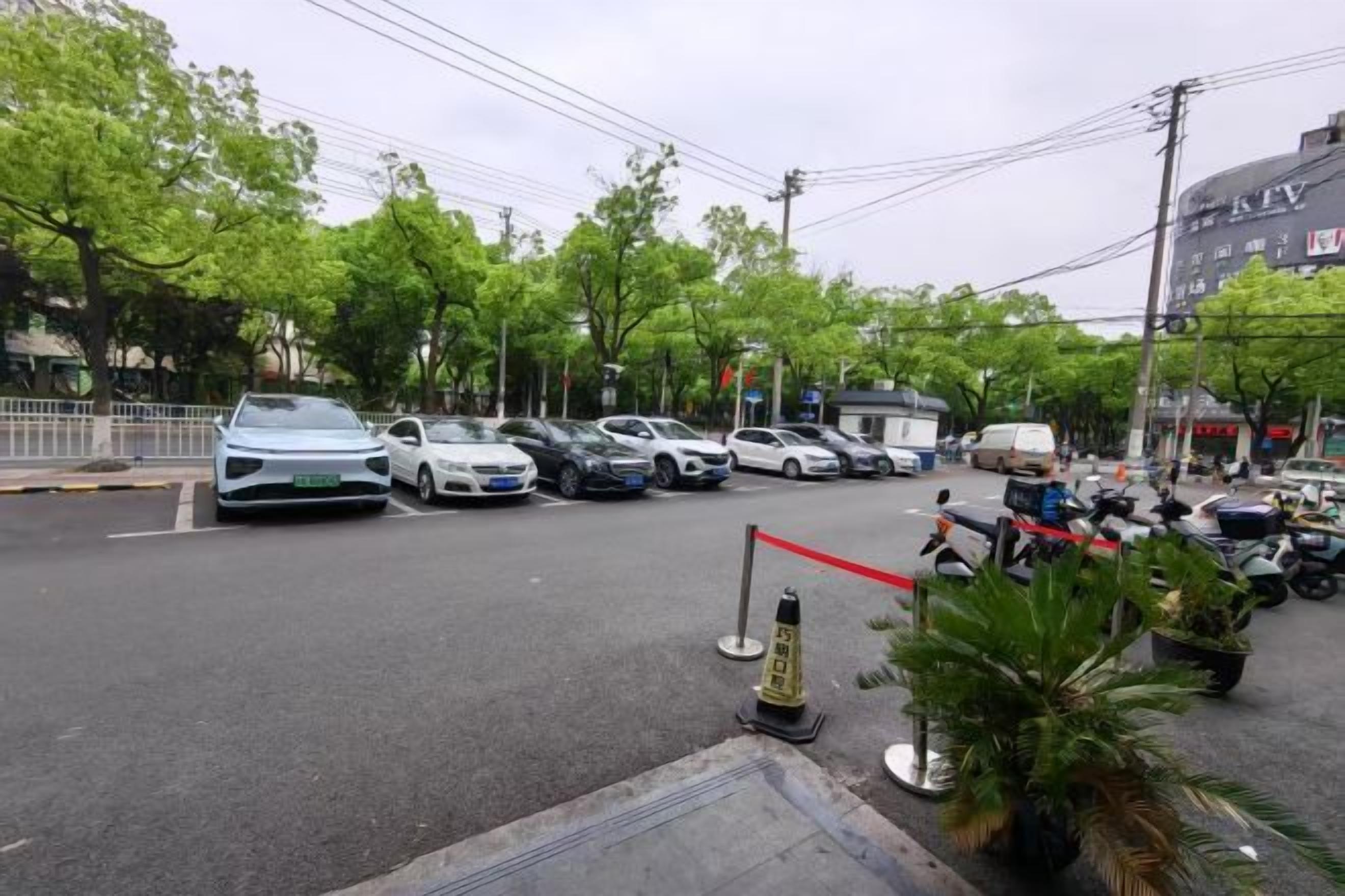 Um estacionamento com vários carros e motocicletas, uma barreira de corda vermelha e um cone de trânsito.