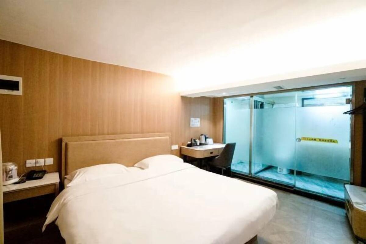 Een hotelkamer met een bed, een bureau, een stoel en een douchecabine met glazen wanden.