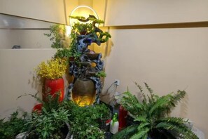 A decorative indoor garden with a tiered water feature, various plants, and a wall-mounted light fixture.