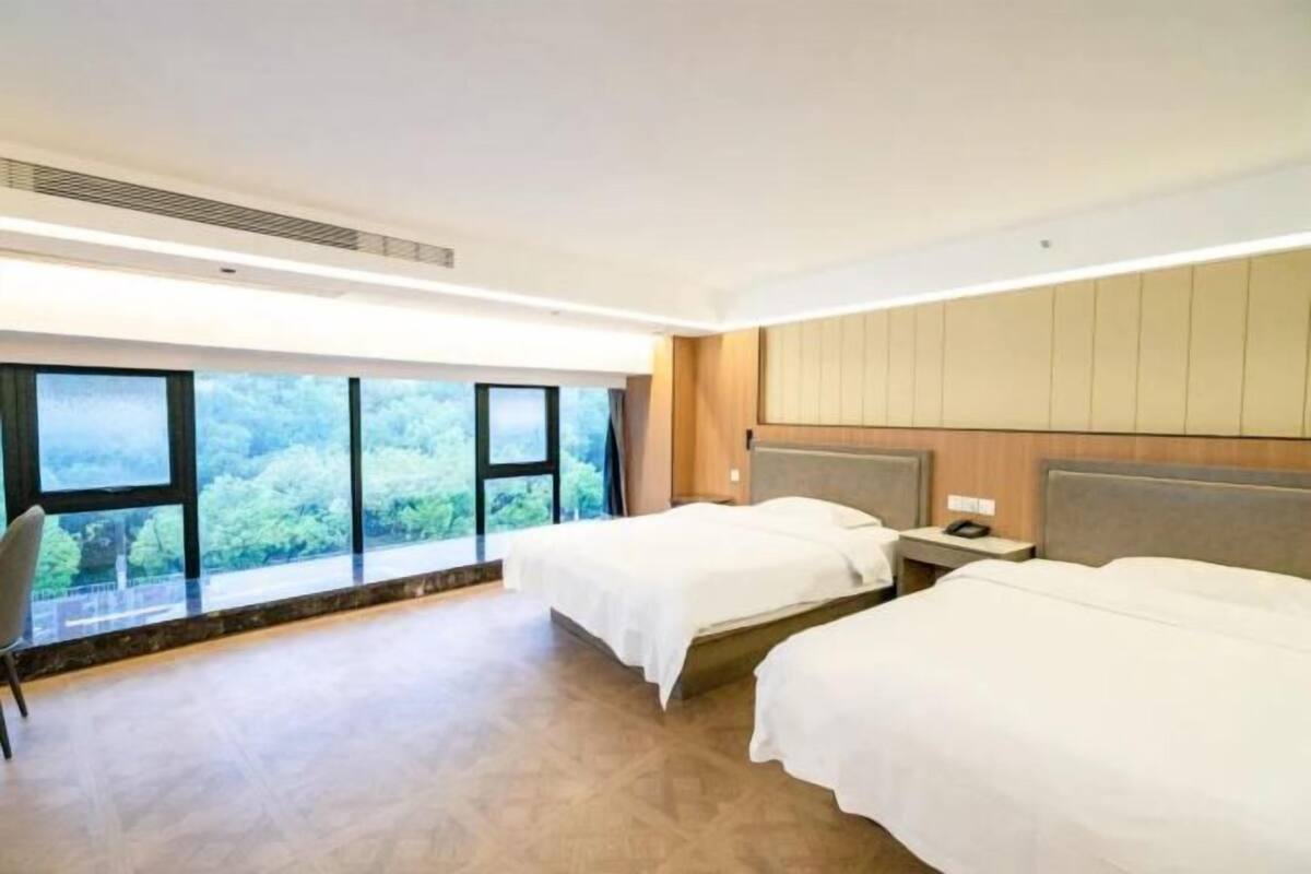 Een hotelkamer met twee bedden, een groot raam en uitzicht op bomen.