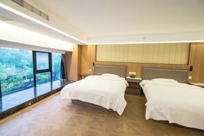 Une chambre d’hôtel avec deux lits, une grande fenêtre donnant sur un paysage verdoyant et une tête de lit en bois.