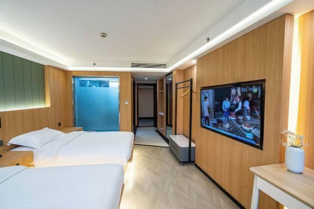 Een moderne hotelkamer met twee bedden, een aan de muur bevestigde televisie en een houten paneelwand.