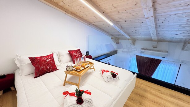 Une chambre d’hôtel avec un grand lit, des poutres en bois au plafond, une petite table en bois sur laquelle sont disposés des éléments pour le petit-déjeuner, et une vue sur le ciel par la fenêtre.