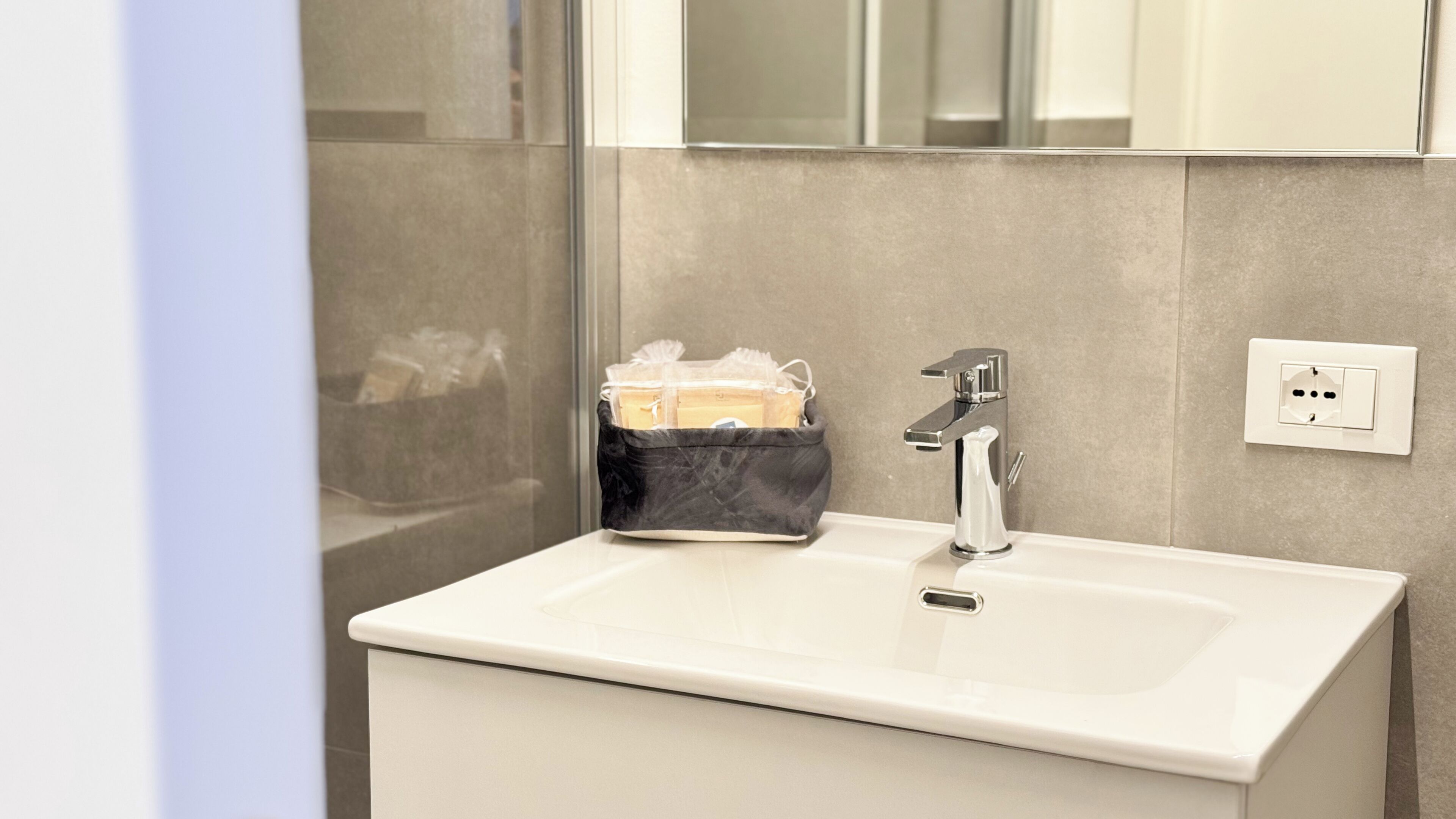 Une salle de bain avec un lavabo blanc, un robinet chromé, une poubelle noire et un miroir.