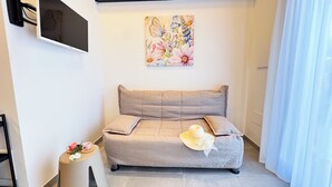 Une pièce chaleureuse avec un canapé beige, une petite table ronde surmontée d’un chapeau et un tableau floral accroché au mur.