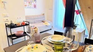 Un coin repas avec une table dressée pour deux personnes, un canapé en arrière-plan et une fenêtre avec des rideaux.