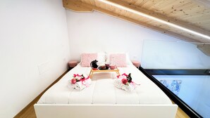 Un lit bien fait, avec une literie rose et blanche, un plateau contenant des éléments de petit-déjeuner, et une fenêtre donnant sur un ciel bleu et des nuages.