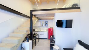 Eine moderne Küche mit einem roten Kühlschrank, einer Mikrowelle und einem Waschbecken. Eine Treppe führt zu einer Dachbodenartige Wohnfläche, wo ein schwarzer Fernseher an der Wand hängt.