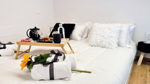 Ein ordentlich bezogenes Bett mit weißer Bettwäsche, ein Tablett mit Frühstücksgebäck und ein Blumenstrauß auf dem Bett.