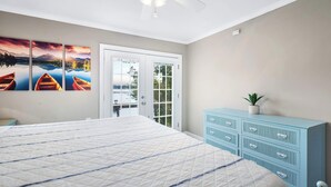 Quarto com cama grande, ventoinha no teto, cómoda azul e porta que dá para uma varanda.