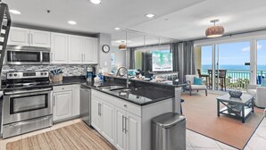 A modern kitchen with stainless steel appliances, a large island, and a dining area with a view of the ocean. - Sterling Shores 616 (Destin)