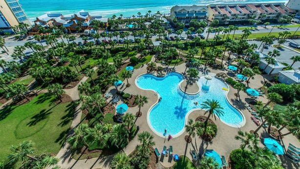 A resort with a large pool, palm trees, and a view of the ocean. - Sterling Shores 616 (Destin)