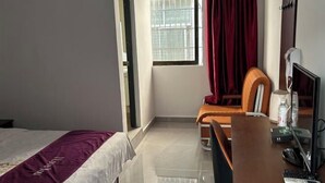 Une chambre d’hôtel comprenant un lit, un bureau avec un ordinateur, une chaise, une fenêtre avec des rideaux et une table de chevet avec une lampe et une bouteille.