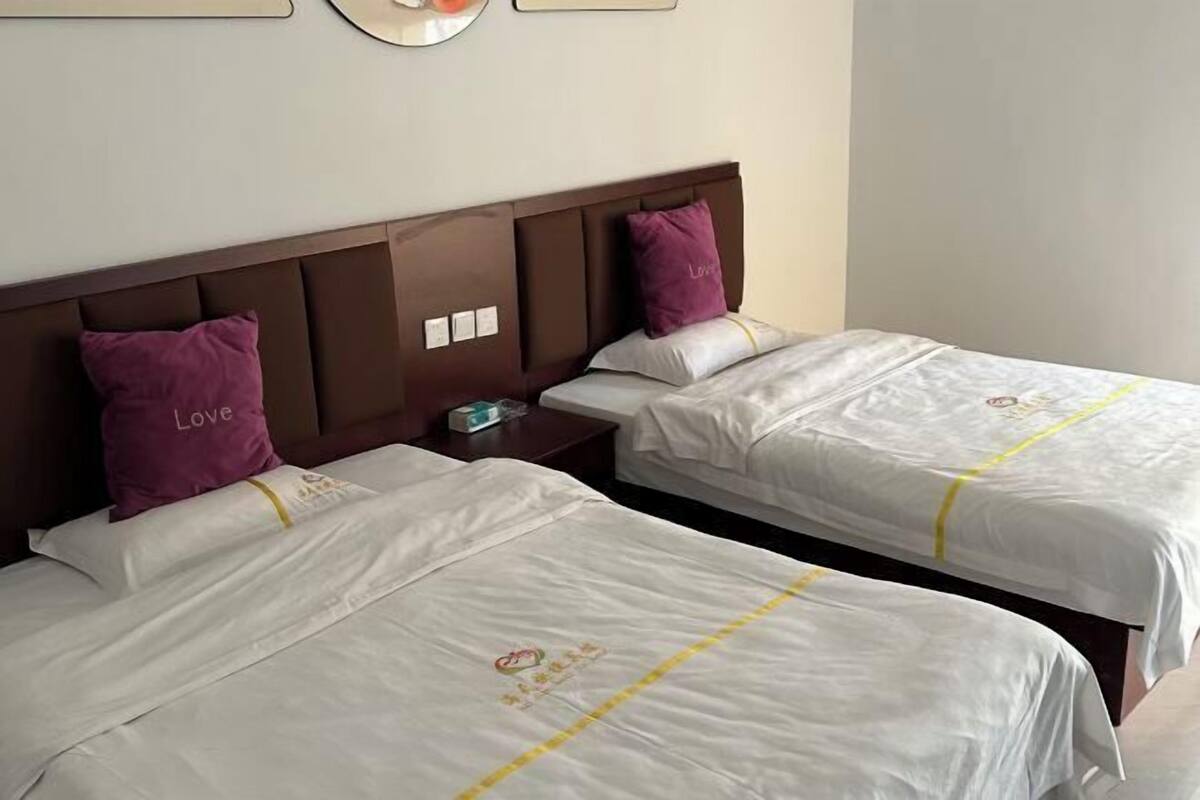 Two twin beds with white linens and purple pillows, a wooden headboard, and a small bedside table with a lamp.