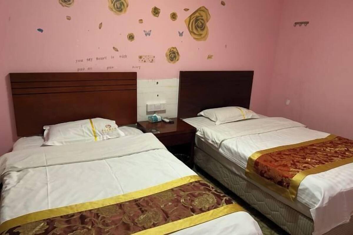 A hotel room with two beds, a wooden headboard, a nightstand, and a wall with decorative stickers.