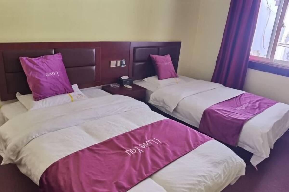 A hotel room with two beds, each with a headboard, a nightstand, and a window with curtains.