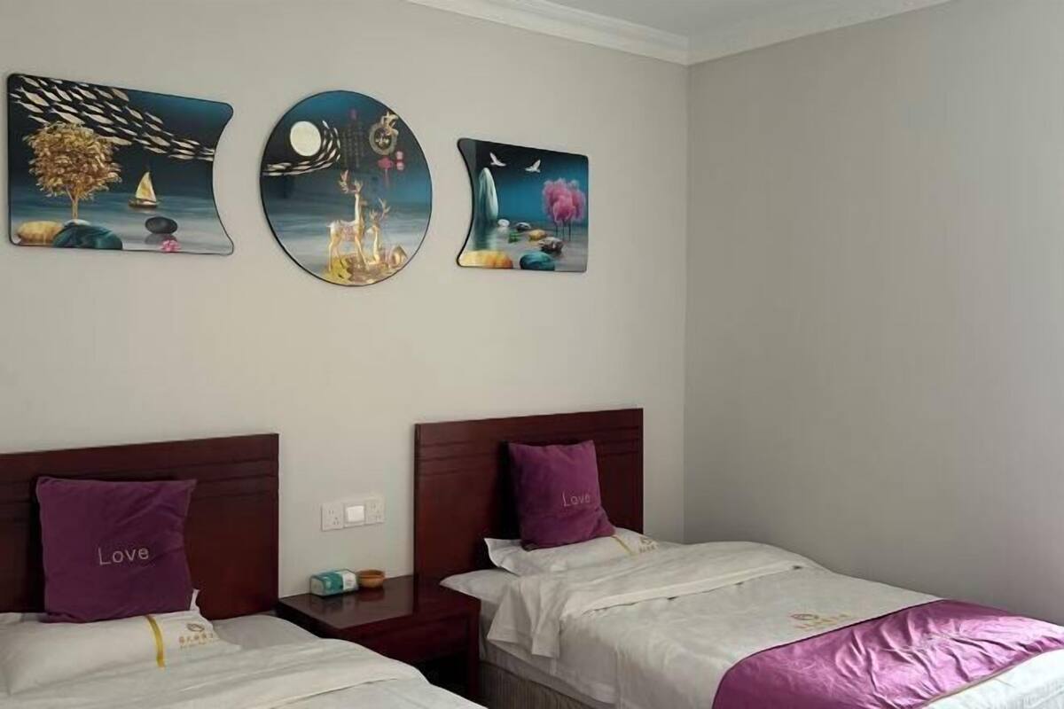 A hotel room with two beds, each with a purple pillow and a white bedspread. There are three wall art pieces depicting surreal scenes.