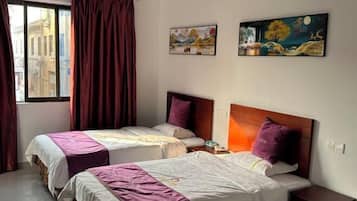 Quarto de hotel com duas camas, uma janela com cortinas e duas pinturas na parede.